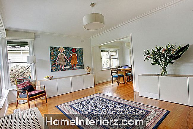 Dzīvojamā istaba ar koka grīdām, dekoratīvs paklājs, violetās lilijas un divu meiteņu glezna