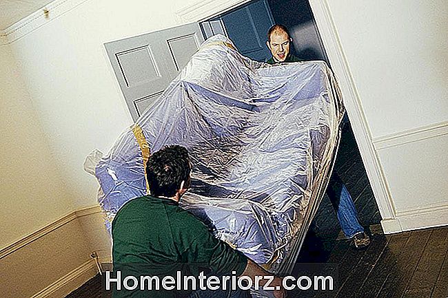 Двое мужчин-мужчин, несущих диван, покрытый пластиком через дверной проем