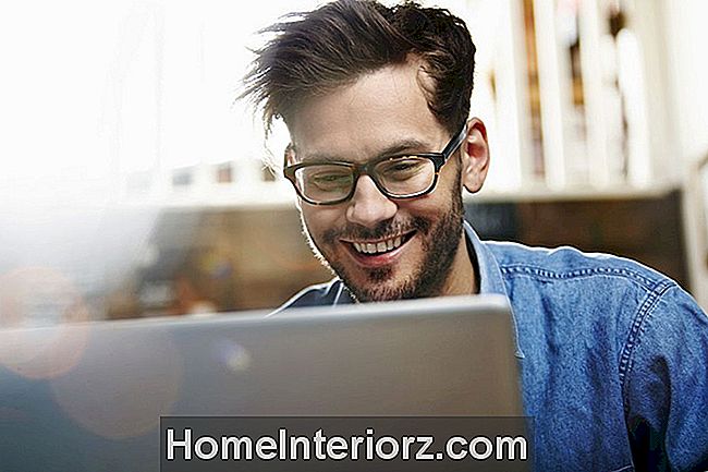 Jaunas vyras su akiniais žiūri į nešiojamą kompiuterį