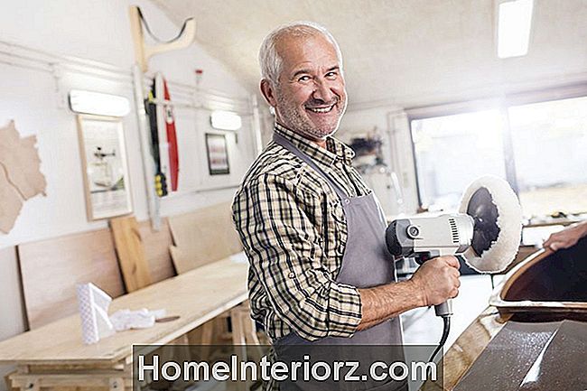 Portrets smaidošs, pārliecināts vecākais vīra galdnieks, izmantojot buferu slīpmašīna uz koka laiva darbnīcā